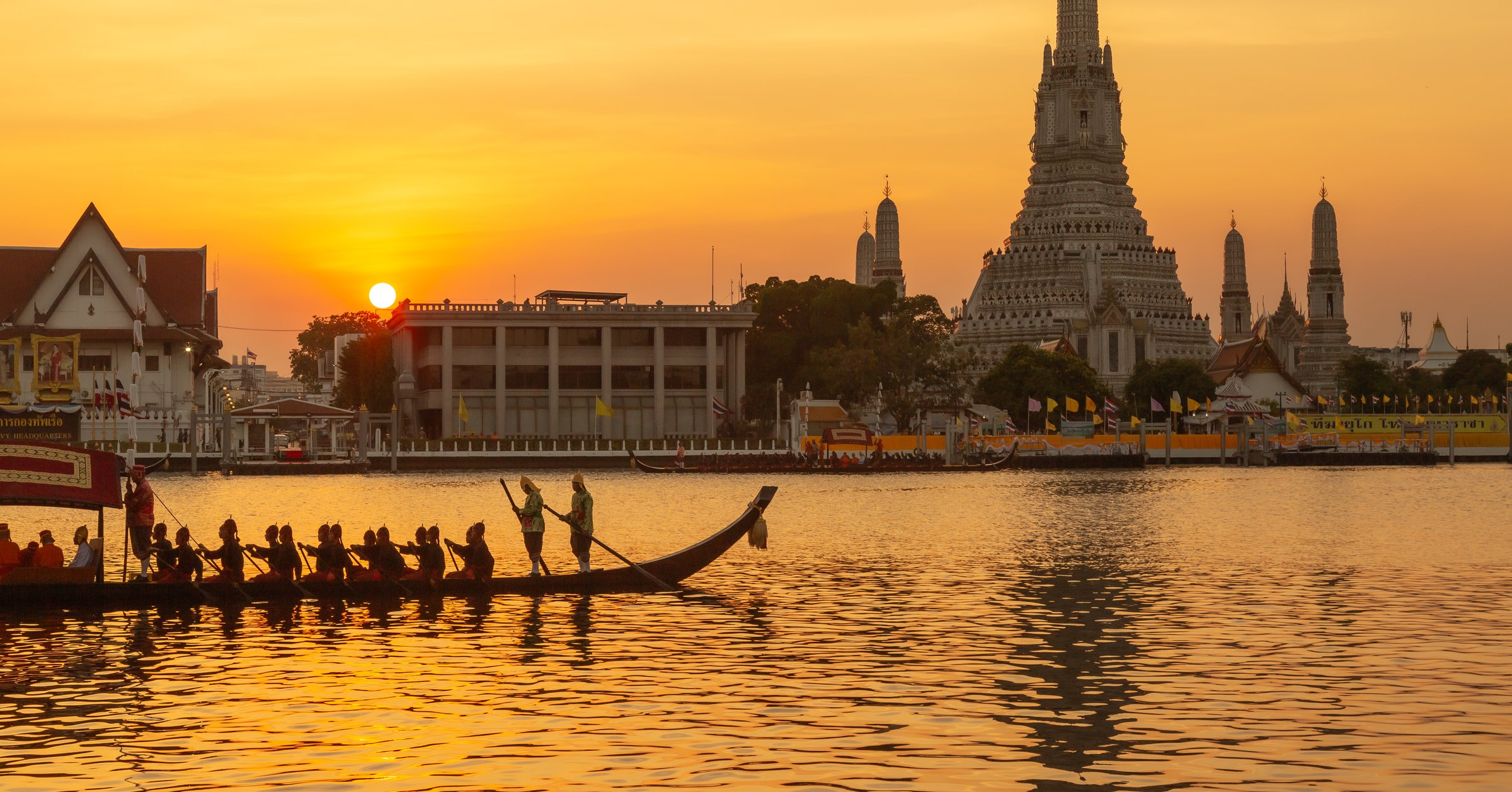 Wat Arun on the Chao Phraya River at sunset with a ceremonial long boat passing in the foreground